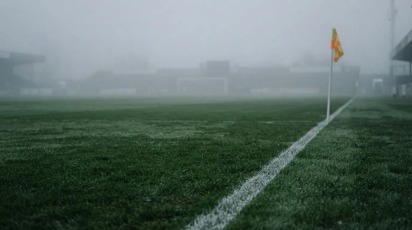 Der Rand eines Spielfelds mit weißer Linie und Eckfahne bei Nebel am frühen Morgen, ohne Menschen.