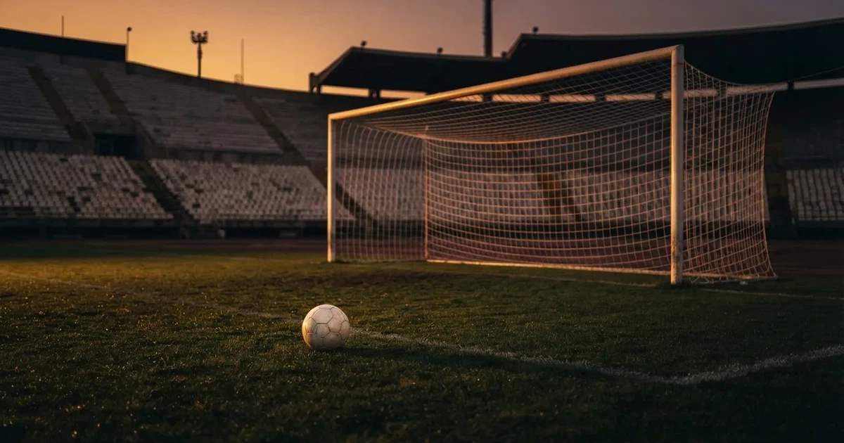 Ein Fußball liegt im Strafraum direkt vor dem Tor mit Netz, im Hintergrund leere Ränge bei Dämmerung.