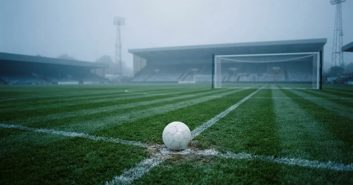 Ein Fußballtor mit gespanntem Netz steht auf einem leeren Rasenplatz, davor ein einzelner Ball, Morgendunst liegt über dem Feld.