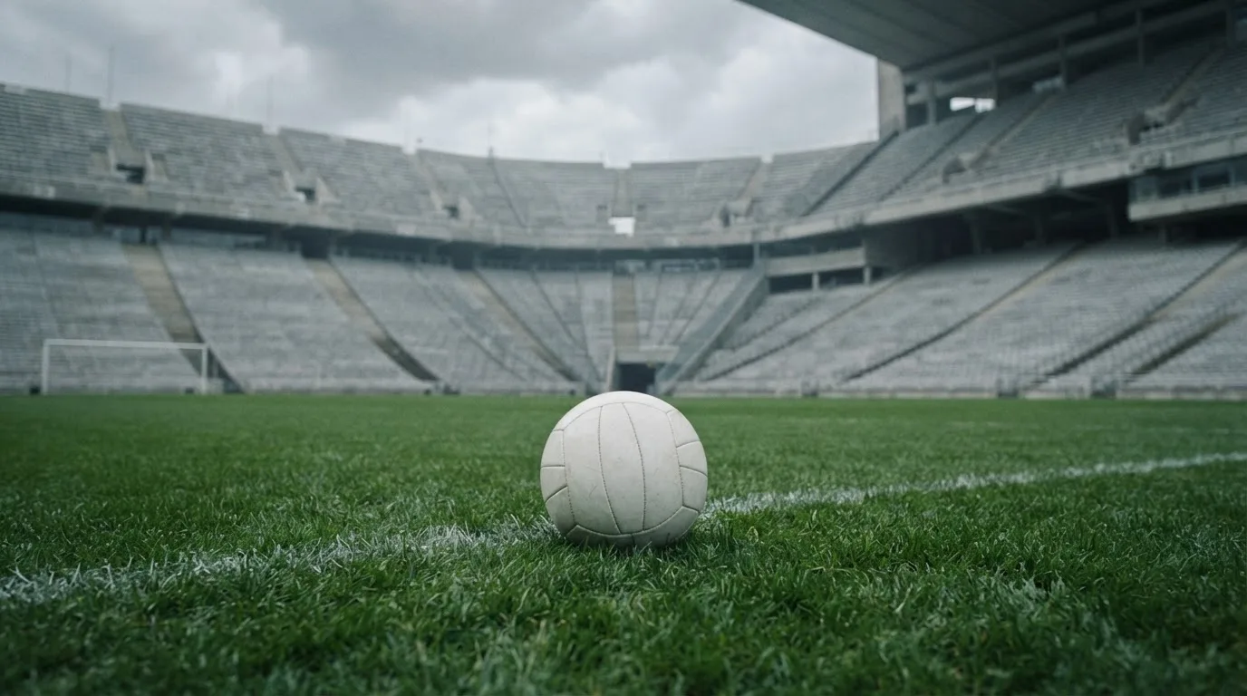 Ein Fußball auf einem Rasen, im Hintergrund ein leeres Stadion bei bewölktem Himmel.