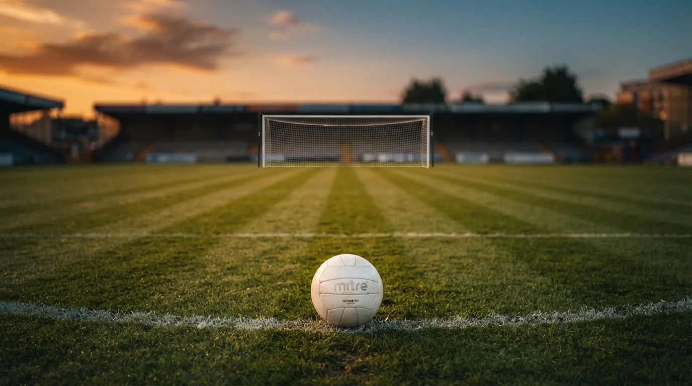 Ein Fußball liegt im Strafraum eines leeren Platzes, dahinter die Netze des Tores im Abendlicht.