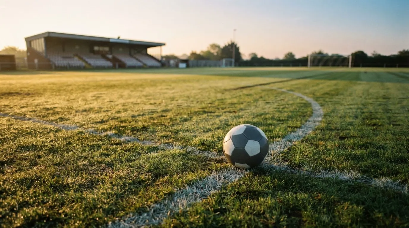 Ein Fußball liegt am Rand des Mittelkreises auf einem leeren Rasenplatz bei Sonnenaufgang.