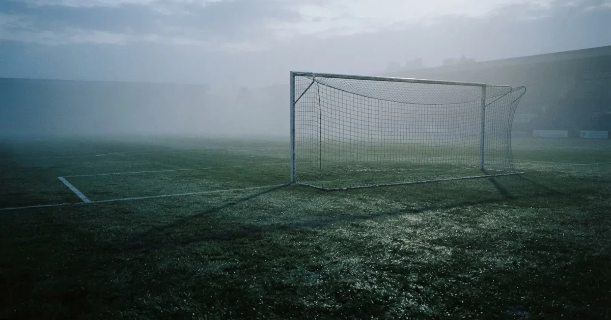 Ein Fußballtor mit Netz steht auf einem leeren Platz im Nebel der Morgendämmerung, der Rasen ist taufeucht.