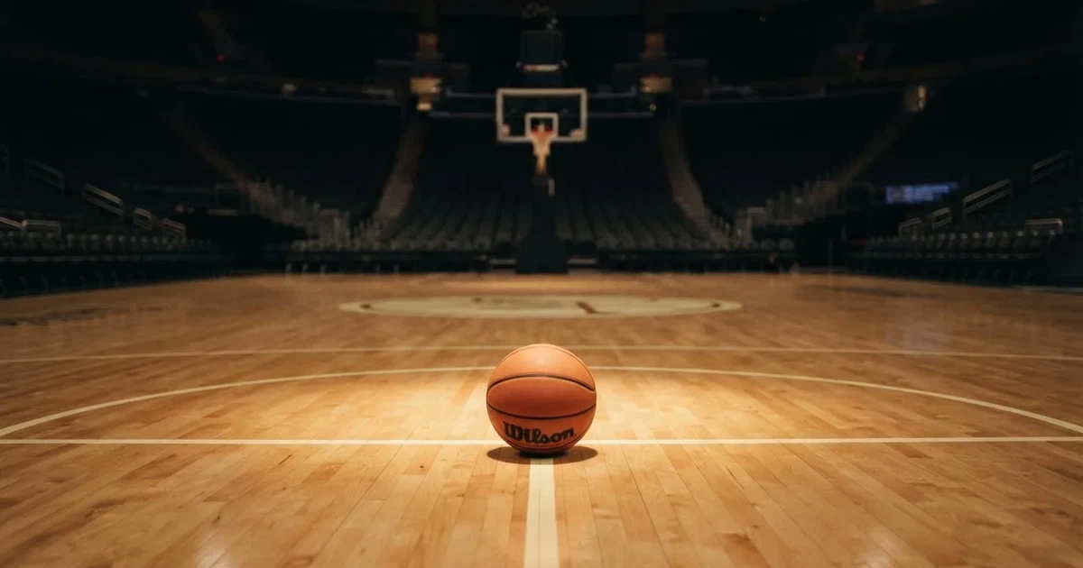 Ein Basketball liegt auf dem Parkettboden einer leeren Arena, Scheinwerfer werfen Licht auf die Mittellinie.