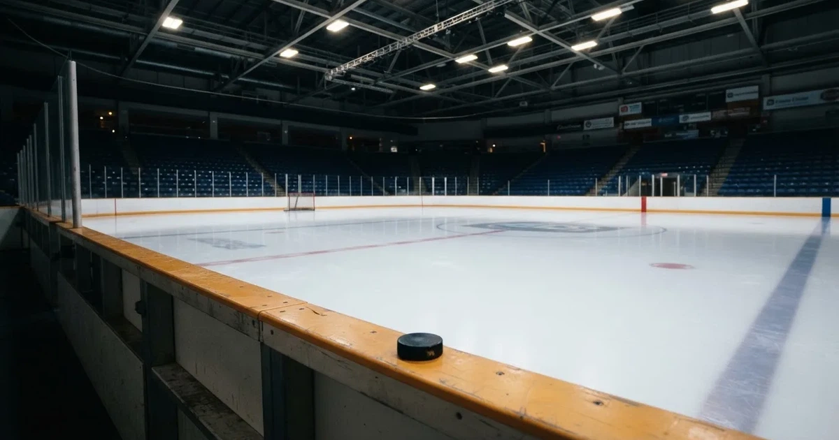 Eine leere Eisfläche in einer Halle mit Banden und Flutlicht, auf dem Eis liegt ein einzelner Puck.