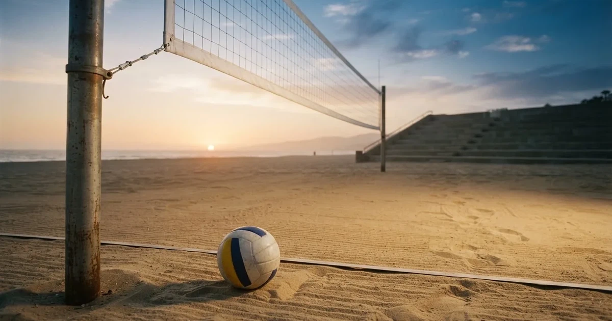 Ein Volleyball liegt auf dem Sand eines Beachvolleyball-Feldes neben dem gespannten Netz, im Hintergrund eine leere Tribüne bei Abendlicht.
