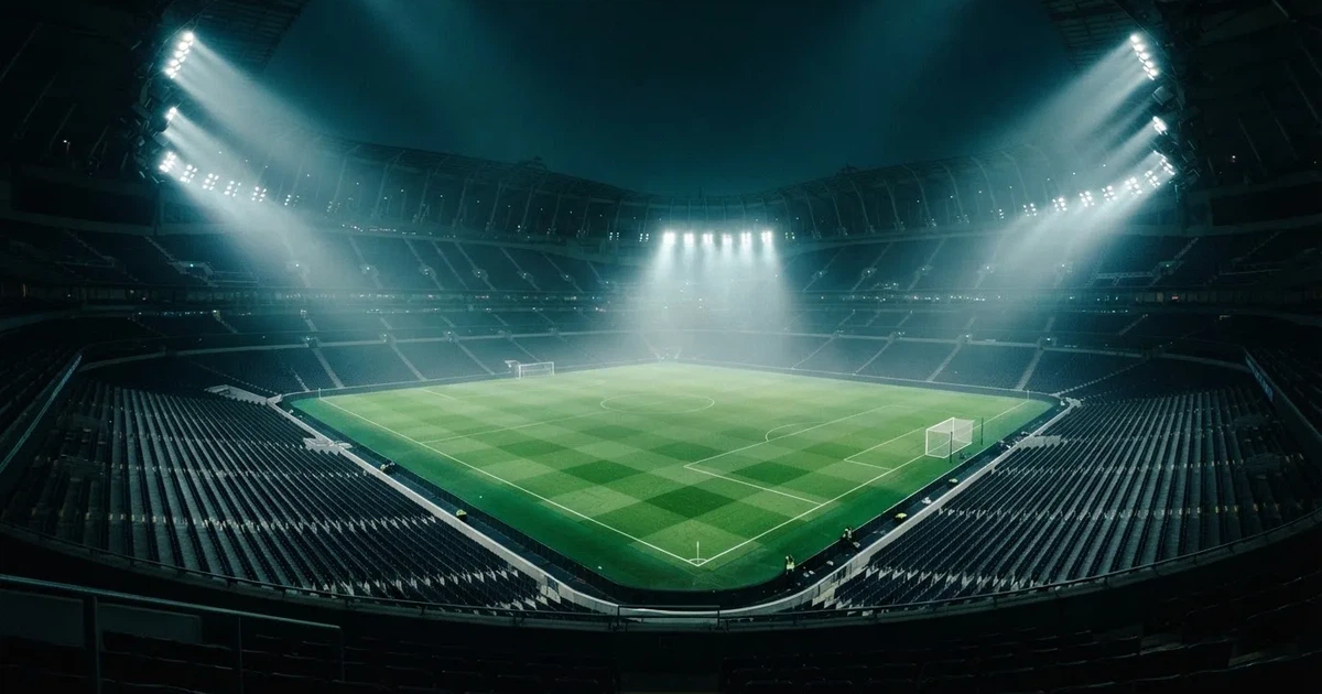 Ein leeres Stadion unter Flutlicht aus großer Entfernung gesehen, Dunst liegt über dem Rasen, die Tribünen sind nur als Lichtpunkte erkennbar.