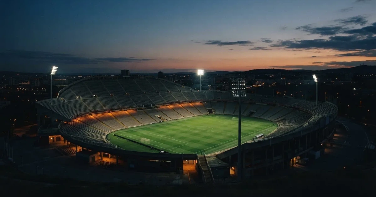 Ein Fußballstadion am Abend unter Flutlicht aus der Ferne gesehen, die Tribünen sind leicht beleuchtet und der Himmel dunkelblau.